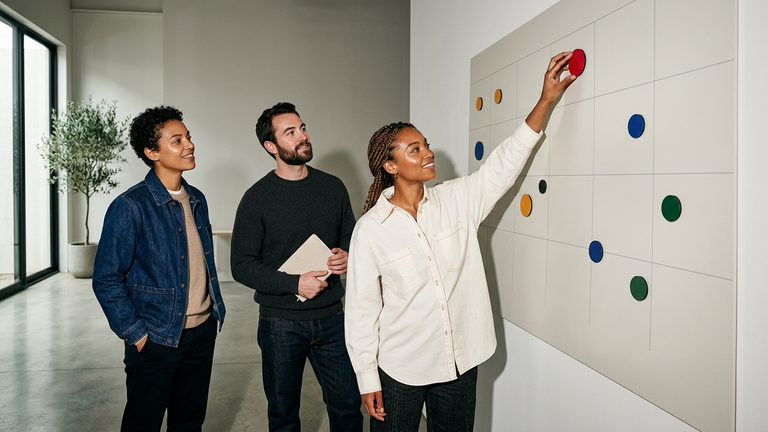 Three colleagues in an office studying a wall planner covered in coloured round markers.